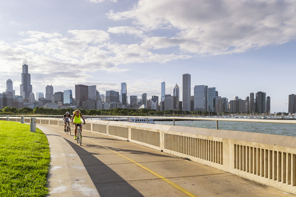Two bikes traveling along the Lakefront Trail next to the lake with the Chicago skyline in the background.