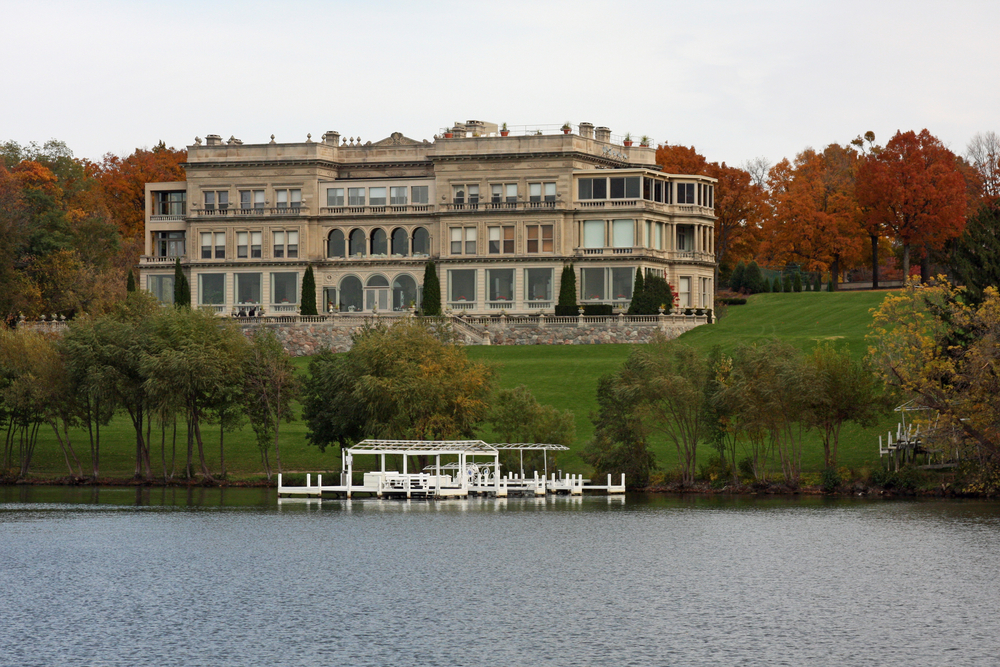 A huge mansion on the shores of Geneva Lake during the fall surrounded by trees with red, yellow, and green leaves. 