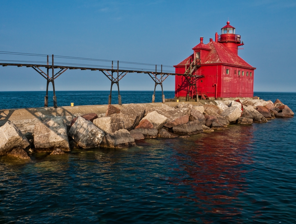 The Breakwater at The Sturgeon Bay Ship Canal Pierhead Lighthouse. A red lighhouse sits at the end of a pier surrounded by water. 