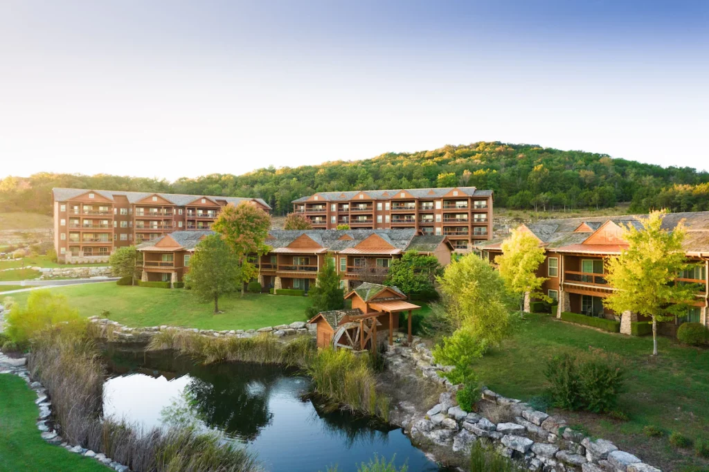 exteriors of a hotel beside a small river with mountains in the backdrop branson family resorts