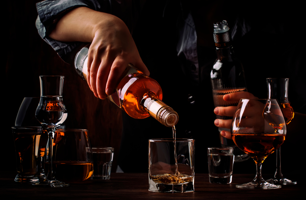 The bartender pours the dark golden rum in glass on the old bar counter. 