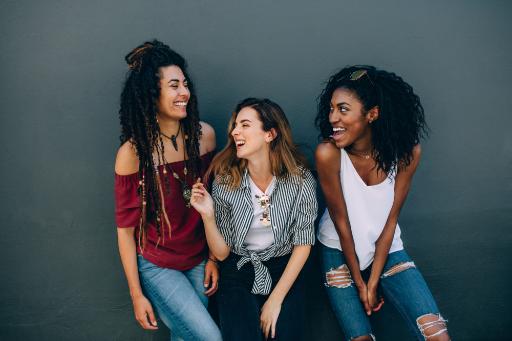 Group of three girl friends leaning on a dark colored wall, wearing great Cleveland outfit ideas.