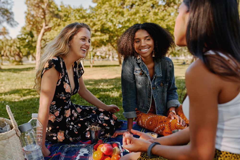 Group of three girls sitting in a park having a picnic.