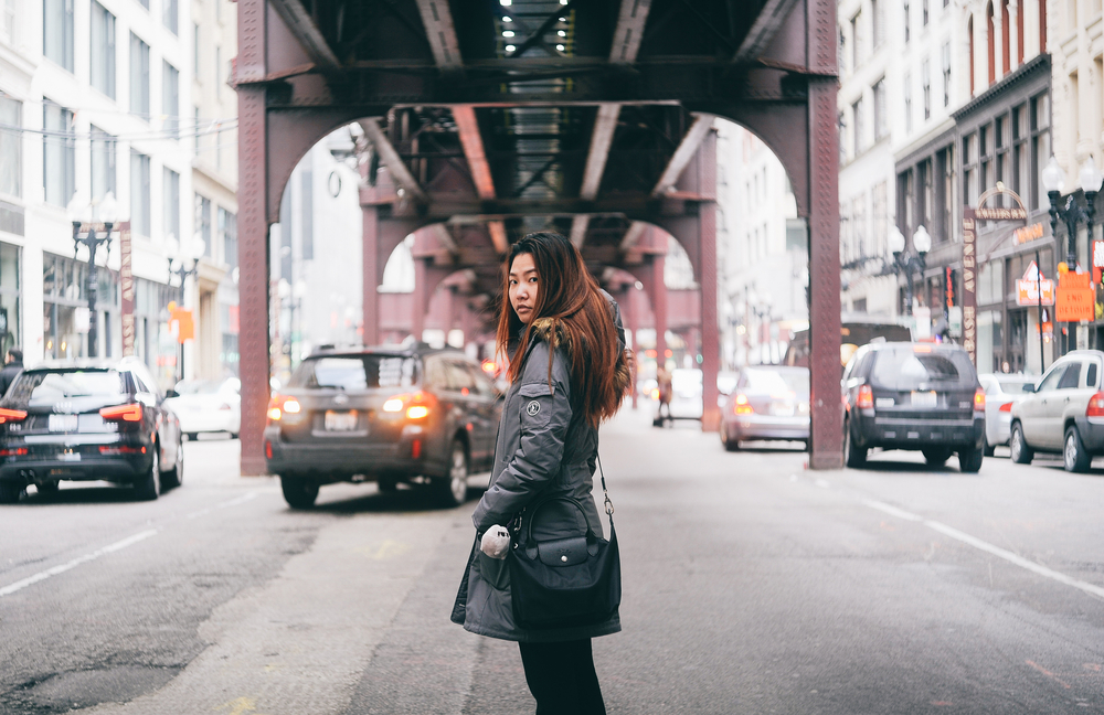 woman in warm jacket standing in the middle of the street under a bridge 