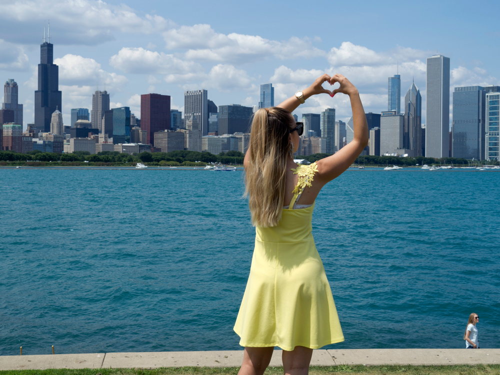 girl making love sign facing towards the water and buildings what to wear in chicago in the summer