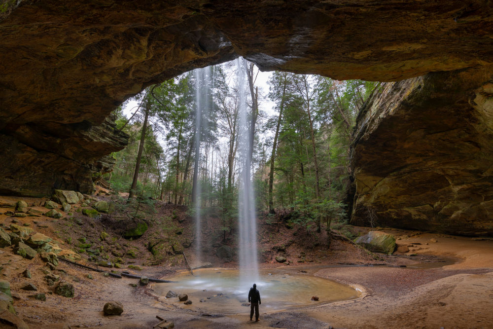 Hiker at Ash Cave in Hocking Hills, Ohio the water in flowing over the cave lip. 