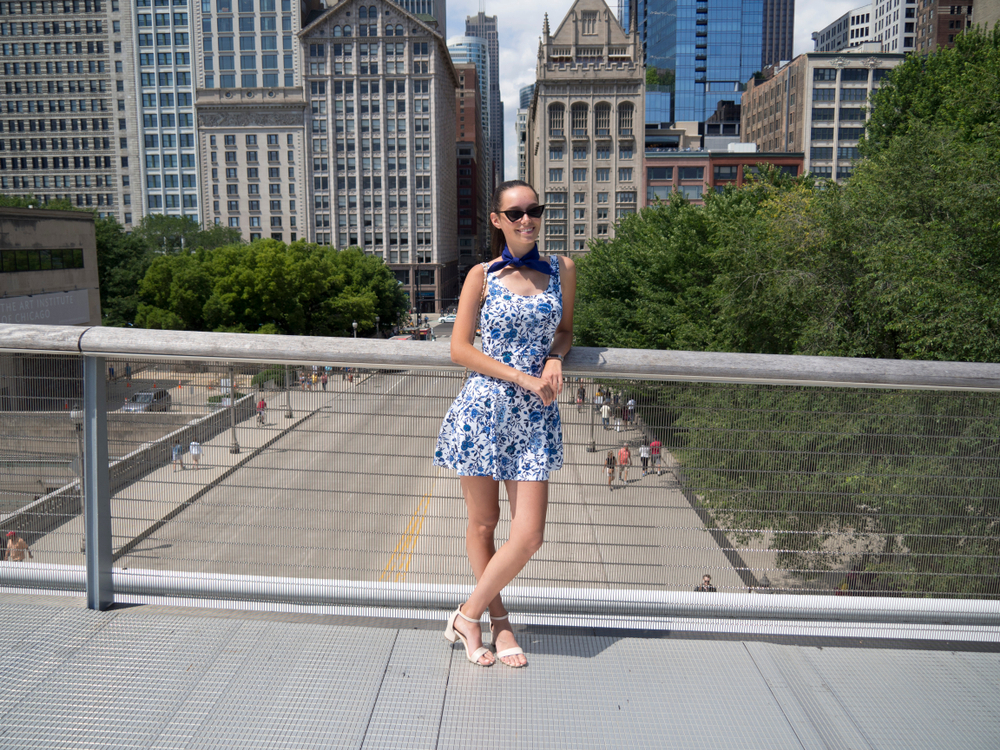 young woman wearing a blue white dress and standing on a bridge in front of buildings