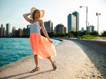 woman wearing grey and orange dress with sunhat beside ocean with buildings in the back what to wear in chicago in the summer