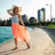 woman wearing grey and orange dress with sunhat beside ocean with buildings in the back what to wear in chicago in the summer