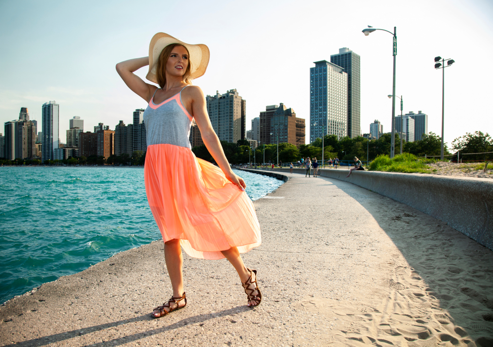 woman wearing grey and orange dress with sunhat beside ocean with buildings in the back what to wear in chicago in the summer