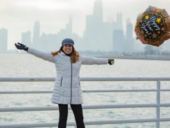 woman smiling in white jacket holding a balloon with Happy New Year in front of the buildings and ocean what to wear in chicago in the winter