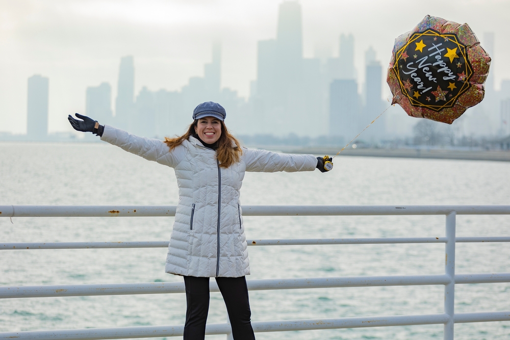 woman smiling in white jacket holding a balloon with Happy New Year in front of the buildings and ocean what to wear in chicago in the winter