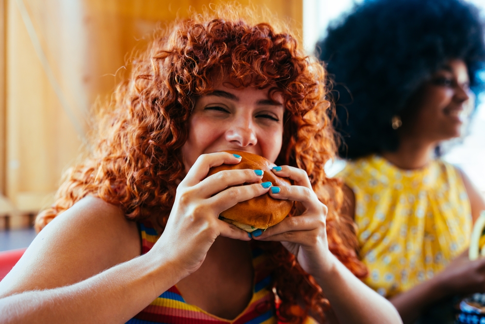 Girl eating burger with friends. It is a close up picture of her face.