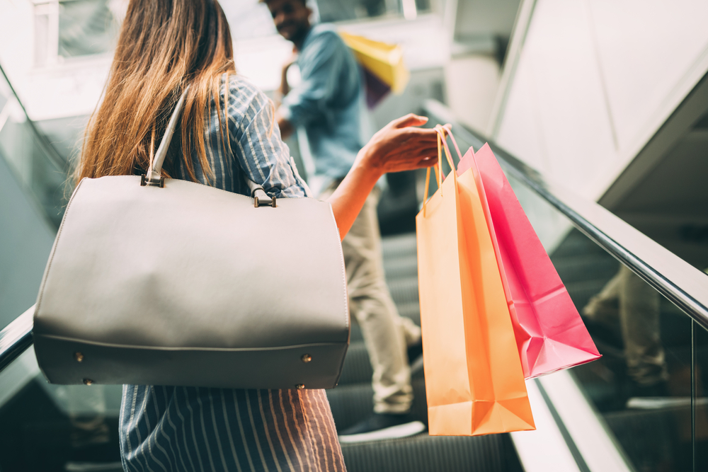 Girl going up escalator holding shopping bags there is a person above her