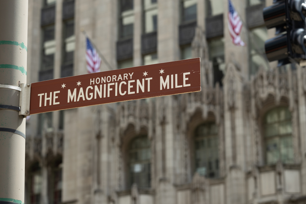 Chicago Magnificent Mile sign with buildings and flags in the background.