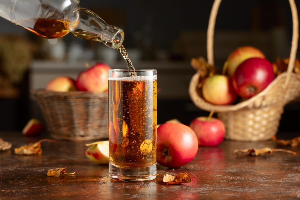 apple cider being poured into a glass on wooden table