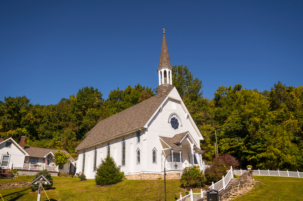 This image shows and idyllic rural, small town church chapel building with trees and a blue sky behind.