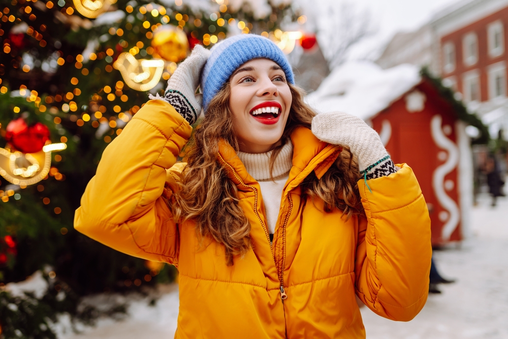 Happy woman in a bright yellow jacket and red lips walks through the Christmas market.