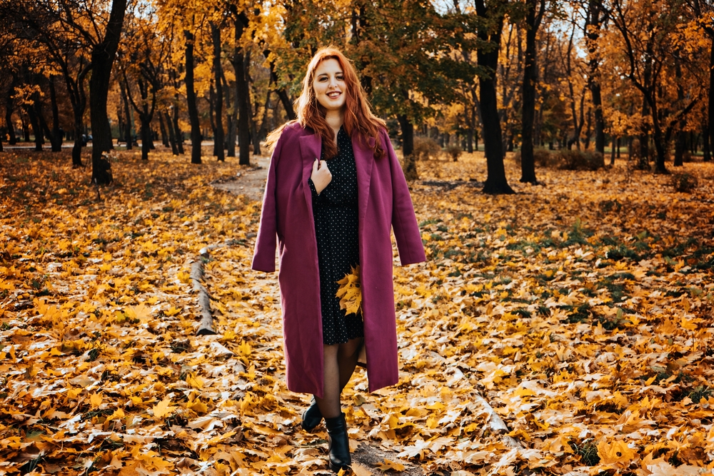 Red hair woman in coat walking in fall park. wearing a coat and dress.