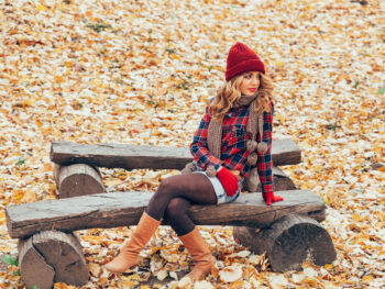 Cacausian woman sitting on log with golden leaves on ground wearing Montana fall outfit.