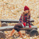 Cacausian woman sitting on log with golden leaves on ground wearing Montana fall outfit.