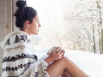 Caucasian woman looking out window at snowy trees