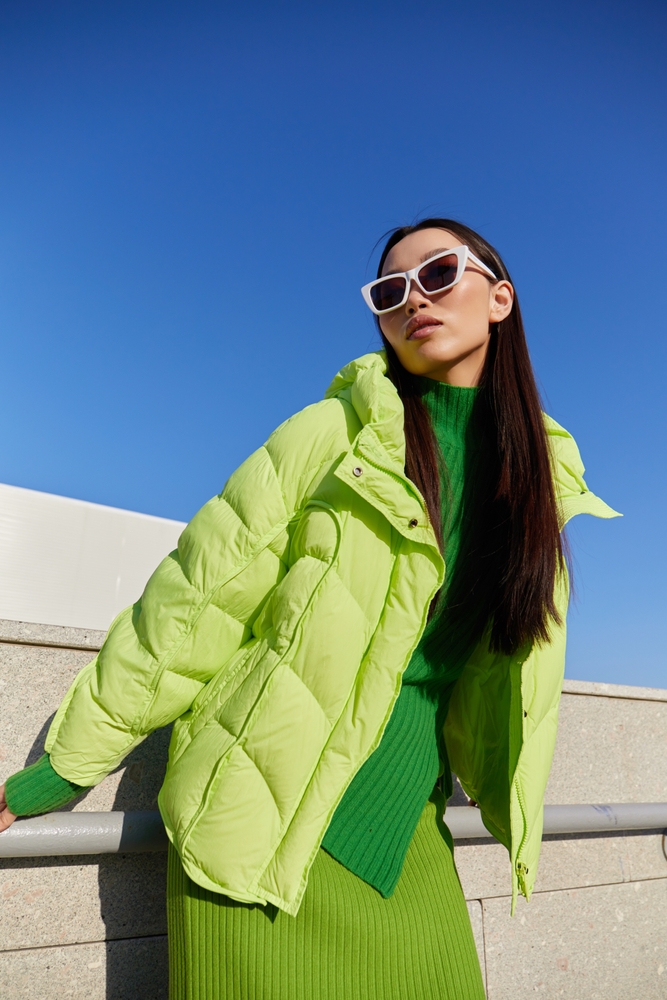 Green down jacket, green skirt, green sweater, sunglasses. Monochromatic look.