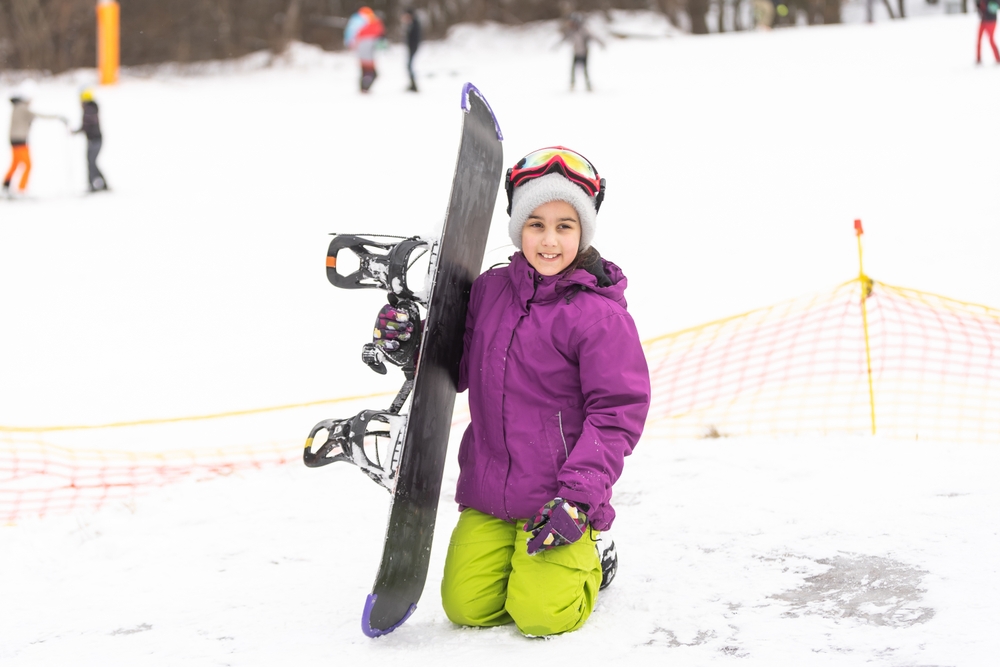 girl sitting on the snow holding a snowboard all inclusive montana ski resorts