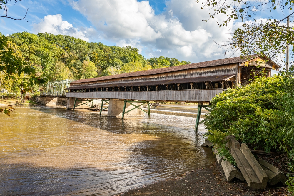 Brown wooden bridge with brown roof spanning wide rust-colored river