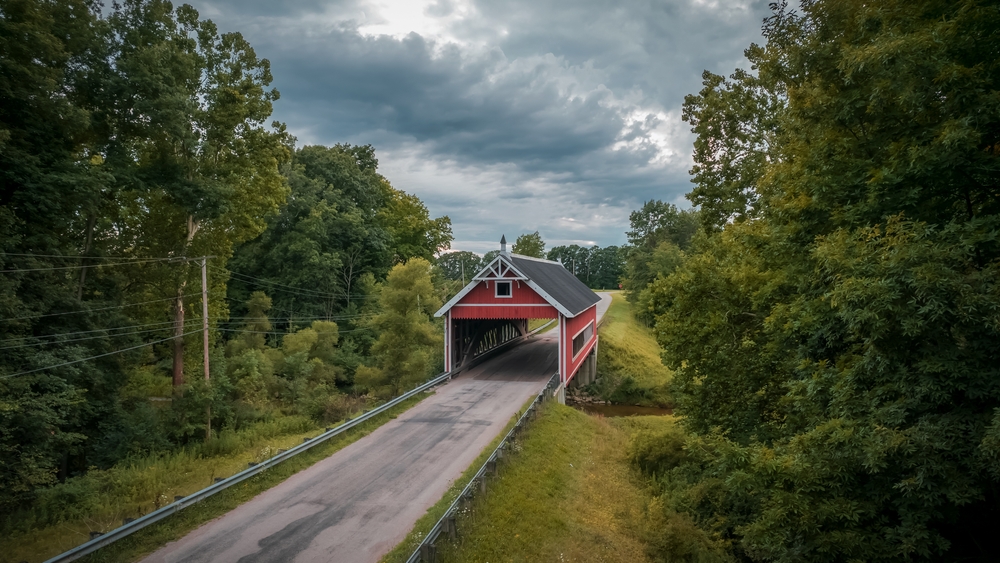 red wooden covered bridge in Ashtabula county Ohio spanning over gully.