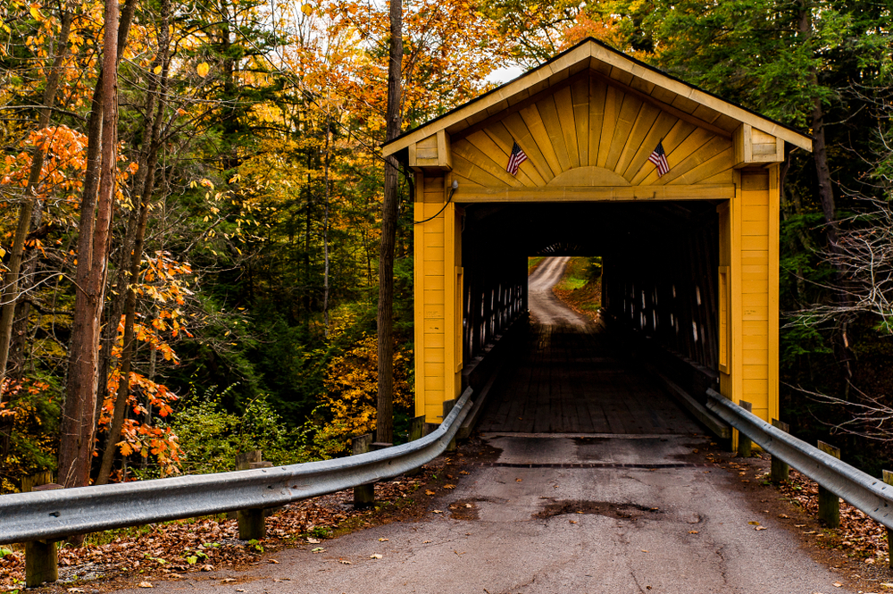 A scenic autumn view of the historic and restored orange wooden bridge surrounded by bright fall leaves.