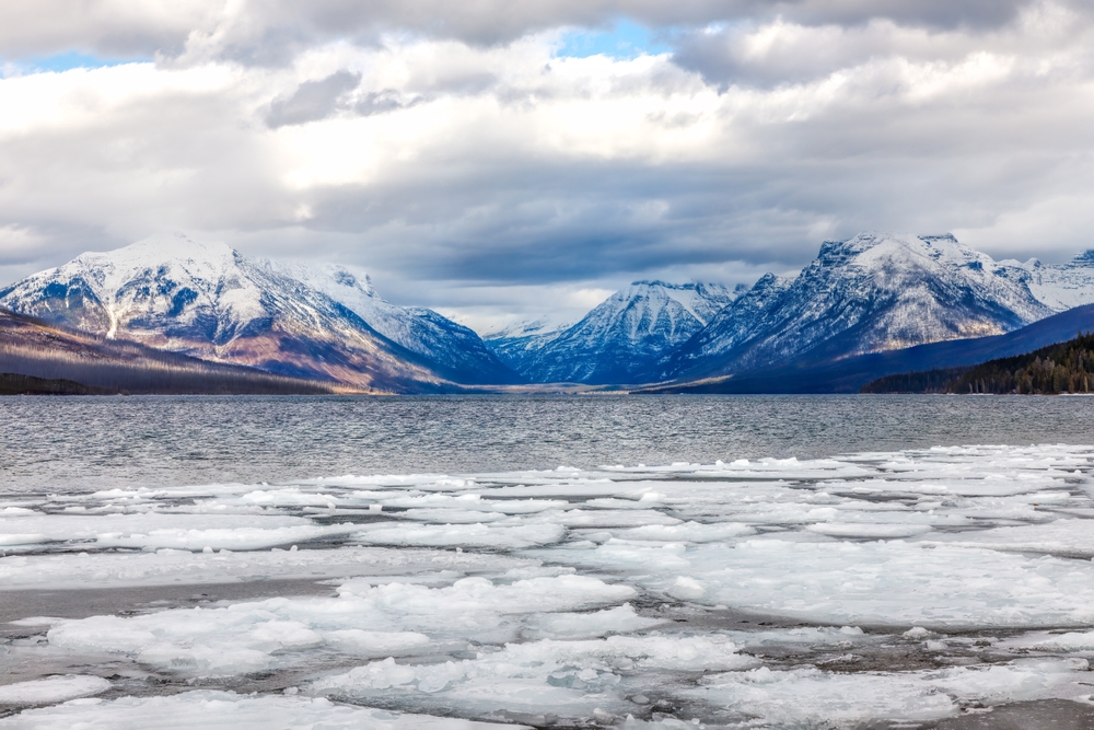 Winter icy scene of Lake McDonald with clouds and majestic mountains. The article is on Glacier National Park itinerary. 