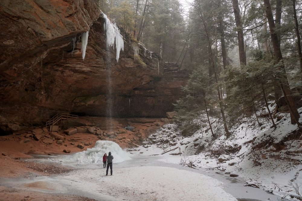 A couple enjoys a moment near the waterfall at Ash Cave in Hocking Hills Ohio.  The article is about Midwest Winter Road Trips.