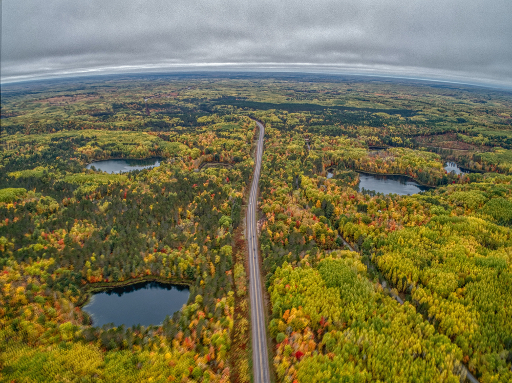 road passing through a forest with lakes during fall season midwest fall scenic drives